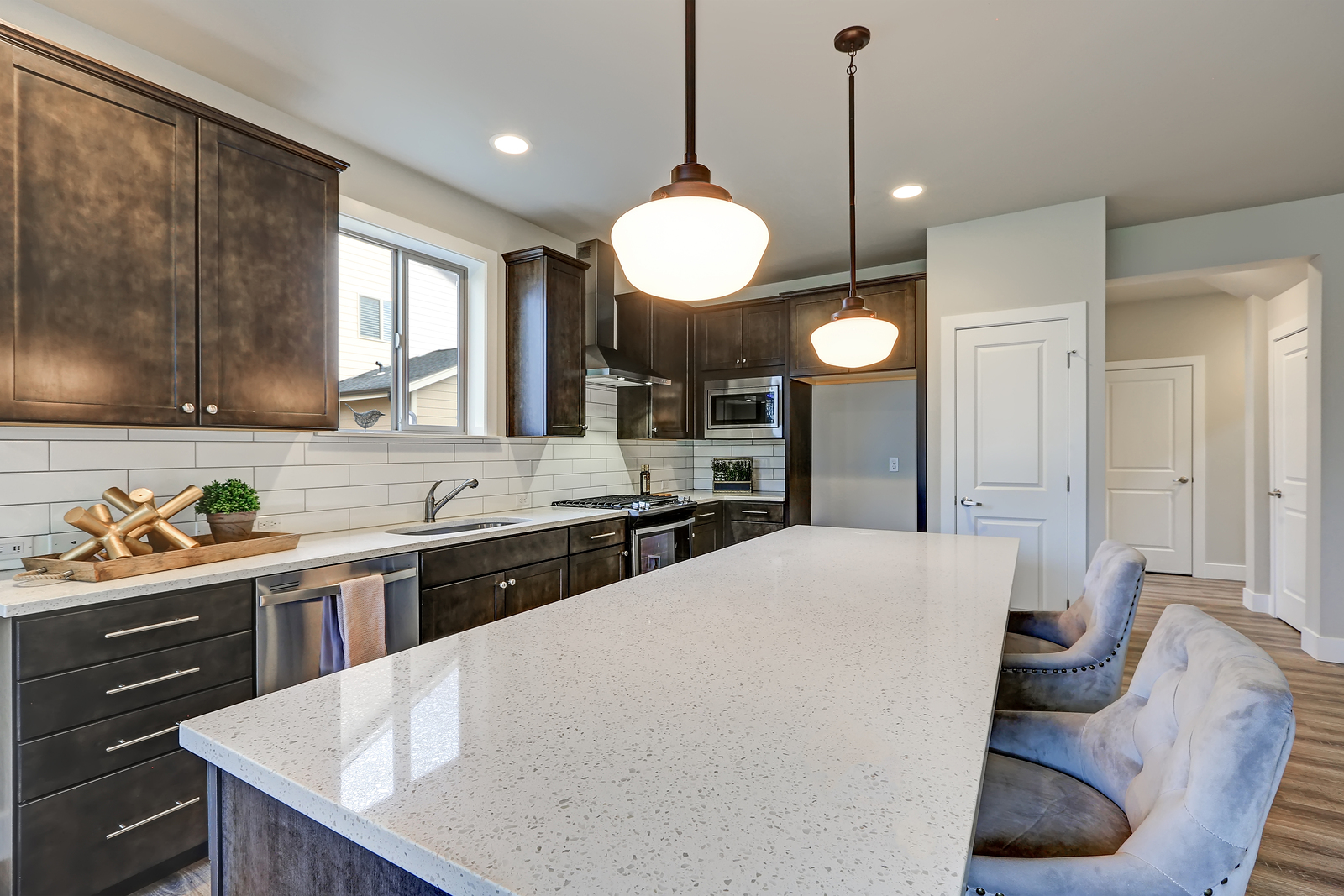 New kitchen boasts dark wood cabinets white backsplash subway tile and over sized island with white and grey quartz counter illuminated by pendant lights. Northwest USA